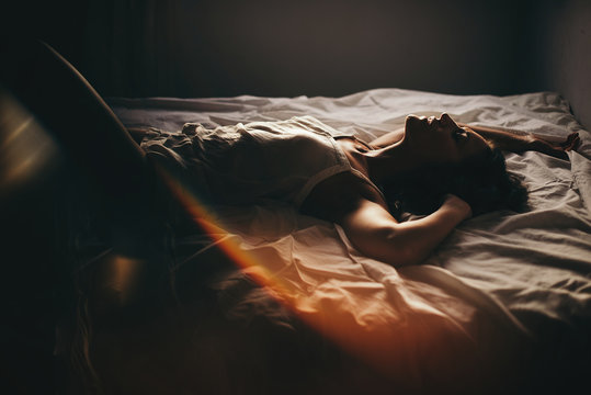 Sensual woman in top lying on bed with eyes closed and arms up
