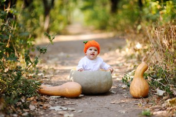 baby girl in the orange cap in the form of a pumpkin sitting inside a huge pumpkin on a background autumn forest. Celebrating Halloween
