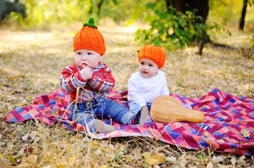 children - a boy and a girl in the orange cap in the form of pumpkins sitting on a plaid blanket on the background of pumpkins and autumn forest