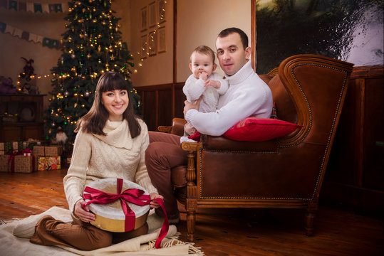Mother, father, son in white knitted sweaters sitting near christmas tree and open gifts