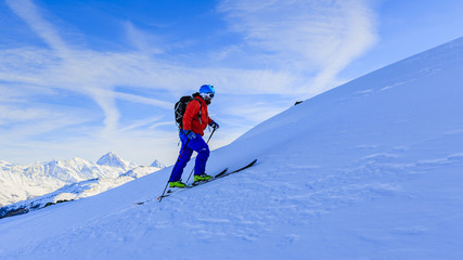 Ski touring man reaching the top at sunrise in Swiss Alps.