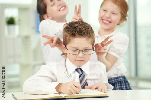 "Two little girls teasing a boy making classwork" Stock photo and