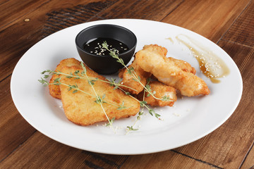 Chicken strips with sauce in a white plate. Wooden background.