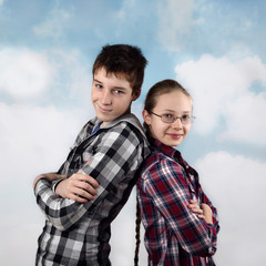 Teenage relationship and friendship - Boy and girl in plaid shirts stand back to back  with happy smiles on cloudy blue sky background