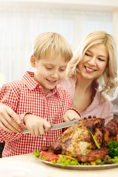 Little boy cutting turkey together with his mother at Thanksgiving Day 