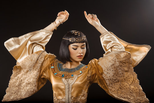 Beautiful woman like Egyptian Queen Cleopatra dancing against black background