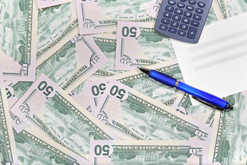 American dollar banknotes laid out evenly with document, pen and calculator over them. Financial desktop background