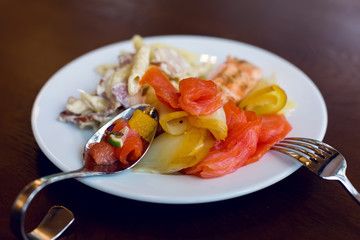 sliced red fish on a white plate  which there are curved steel fork and  spoon