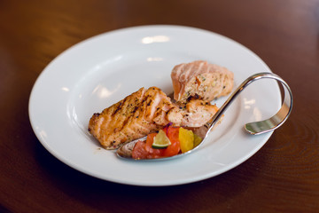 sliced red fish on a white plate which there are curved steel fork and spoon