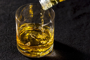 Serving a glass of whiskey, on dark tabletop