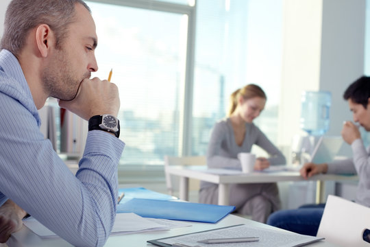 Pensive Man Working In Office With Other Office People