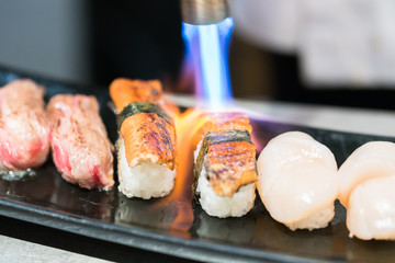 Man's hand holding torch burner. Chef prepares  sushi.
