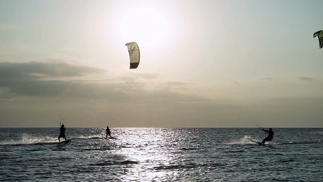Kitesurfing. Six kitesurfers going surfing on the surfboards on waves at sunset. HD