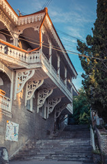  A view of the beautiful wood painted white details in architecture. Extremely ornate windows and balcony, vintage building, green trees and stair, sunny morning, oriental style.
