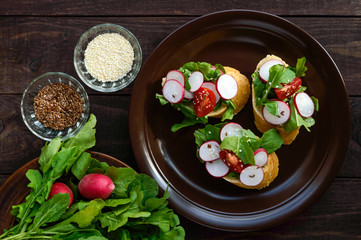 Fitness Vegetarian sandwiches with radish, cherry tomatoes, arugula, sesame, flax seeds, white crispy baguette. The top view. Dark Wooden background