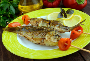 Fried fish (carp) on skewers with pieces pepper and lemon.