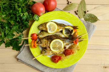 Fried fish (carp) on skewers with pieces bell pepper, sun-dried tomatoes and lemon. The top view
