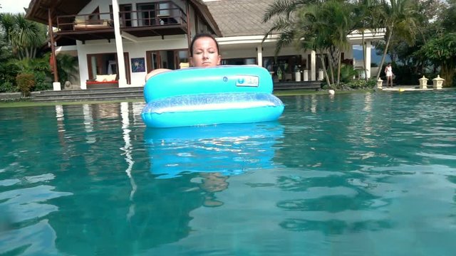 Young woman sunbathing on air mattress in swimming pool, super slow motion 240fps
