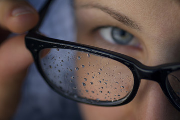 Girl with a vision problem, looks through the glasses. Glasses covered with drops of water (rain).