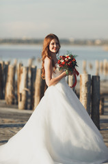Fototapeta na wymiar Beautiful young bride with bridal bouquet posing on the background sea