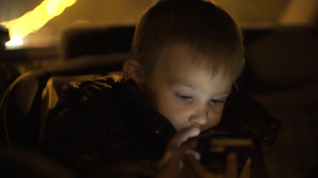 Little boy watching cartoon on phone sitting in baby car seat
