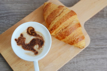 cup of cappuccino and yummy croissant on wooden table
