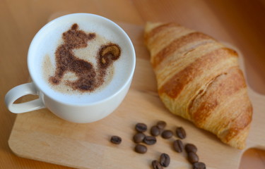 cup of cappuccino and yummy croissant on wooden table
