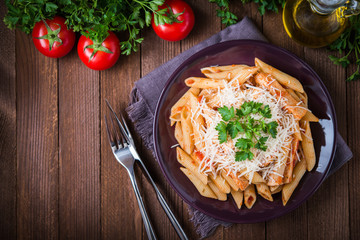 Penne pasta with chicken, tomato sauce, parmesan cheese and parsley on dark wooden background top view. Italian cuisine. Space for text.