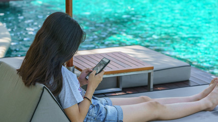 Asian teenager relaxing and playing mobile phone beside swimming