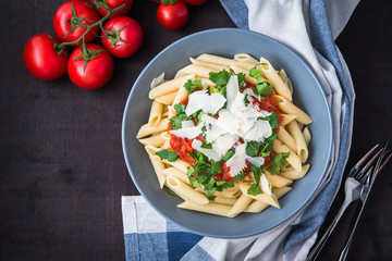 Penne pasta with tomato sauce, parsley and parmesan cheese on black wooden background top view. Italian cuisine.