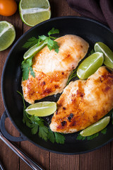 Chicken breasts with lime and parsley on dark wooden background top view. Healthy food. Nutritious meal.