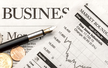 Pen with coins on the business newspaper.