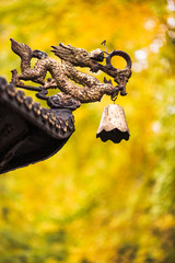 Dragon sculpture with a bell on a roof of a chinese temple with yellow leaves from autumn trees in the background