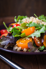 Fresh healthy salad with quinoa, cherry tomatoes and mixed greens (arugula, mesclun, mache) on wood background close up. Food and health. Superfood.