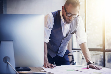 Bearded Businessman Analyzes Business Plan Document Modern Workplace Wood Table.Young Man Working Startup Strategy Desktop Computer.Using Pen Making Note Paper.Guy Work Office.Blurred Sunlight Effect.