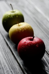 Red green yellow apples in a row with water drops on black wooden table, back light