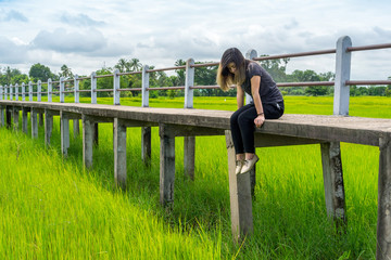 Asian woman sitting on concrete pathway in rice field