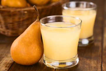 Pear juice in glass with Bosc pear on the side on dark wood (Selective Focus, Focus on the front rim of the glass)