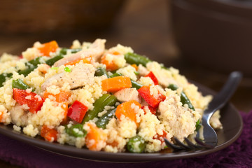 Couscous dish with chicken, green bean, carrot and red bell pepper served on plate with fork on the side (Selective Focus, Focus one third into the dish)