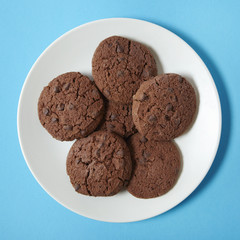A plate of chocolate chunk cookies on a bright blue background
