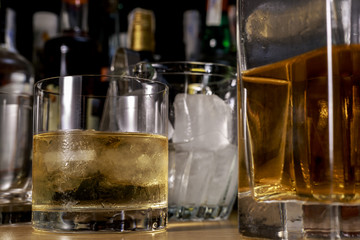 Whisky glass between bottles of different alcoholic drinks