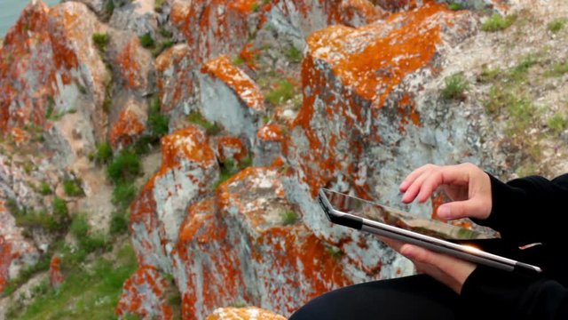 Girl's hands using a tablet PC on the rock, Olkhon Island, Lake Baikal