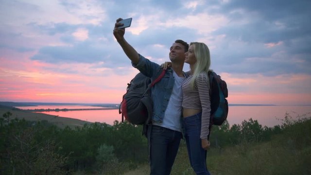 Couple with backpacks smiling making selfie on hill at sunrise Slow motion