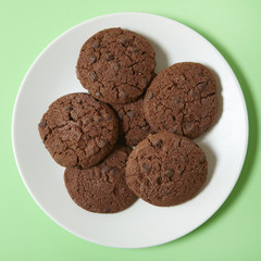 A plate full of chocolate chunk cookies on a pastel green background