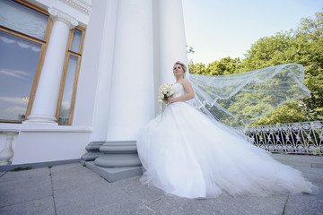Obraz premium Beauty bride in bridal gown with bouquet and lace veil on the nature. Beautiful model girl in a white wedding dress. Female portrait in the park. Woman with hairstyle. Cute lady outdoors