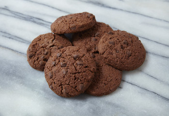A pile of freshly baked chocolate chip cookies on a white marble background