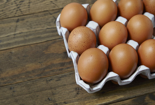 A tray of freshly laid brown chicken eggs on a rustic wooden background forming a page border