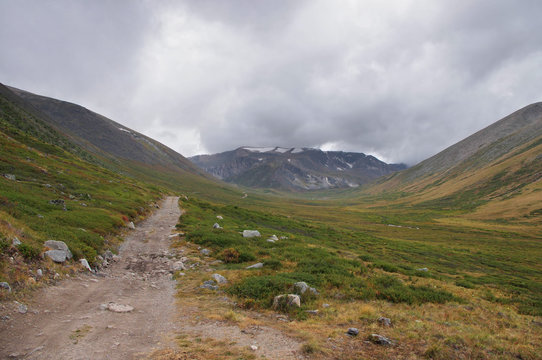 Extreme rocky road in a mountain valley to the pass in cloudy weather on the background of snowy mountain ranges Plateau Ukok Altai Siberia Russia