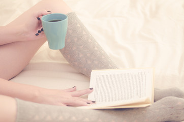 Fototapeta na wymiar WOMAN ENJOYING BOOK AND COFFEE ON BED