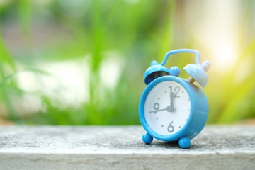 Blue alarm clock on concrete floor with green blurred background